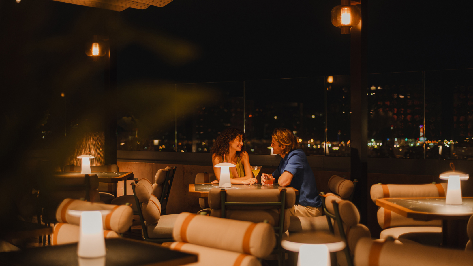 A couple enjoys a romantic evening at an outdoor table, enjoying the urban view at night