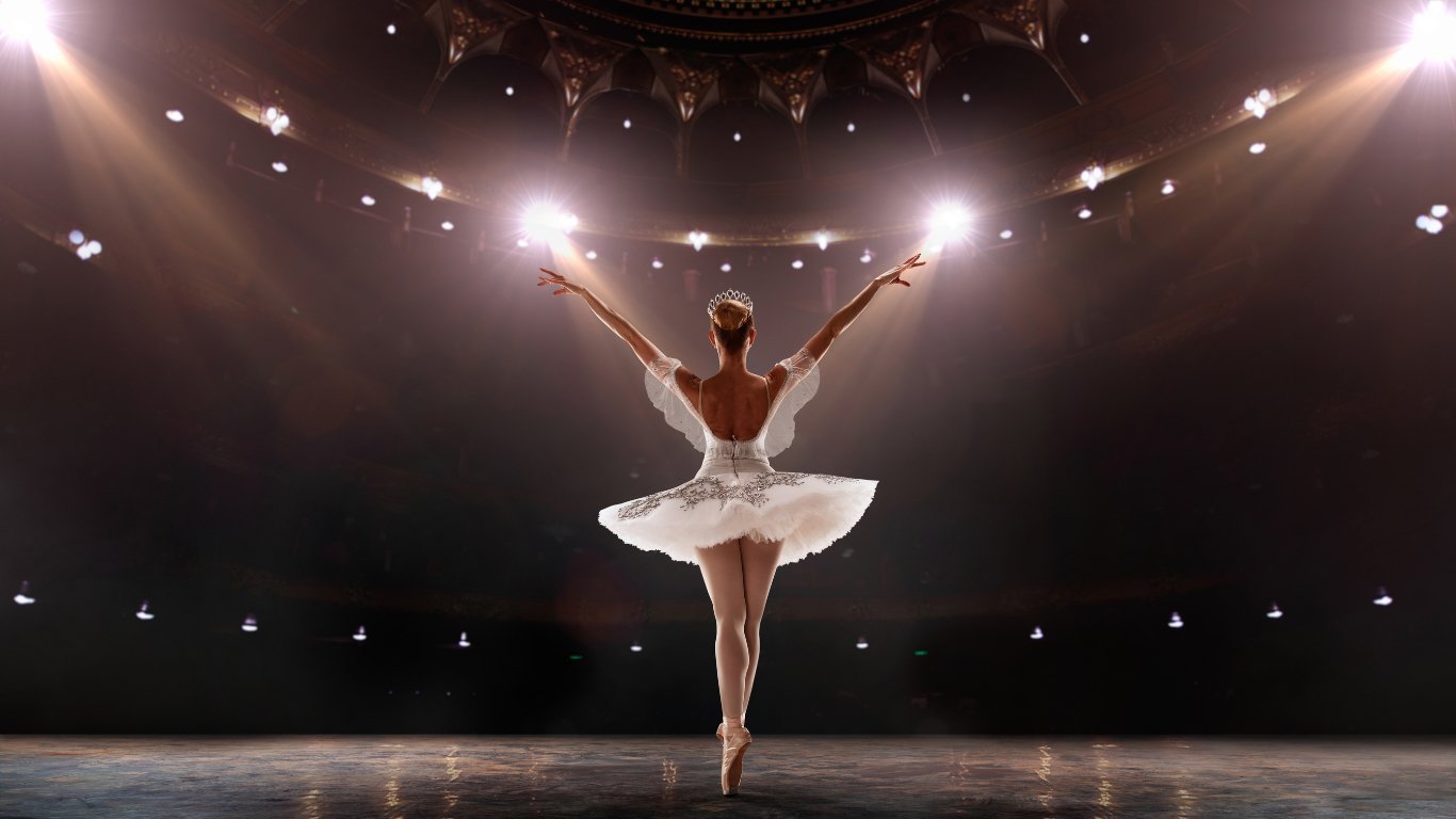 A ballerina in a white dress gracefully poses on stage, showcasing her elegance for the Atlanta Ballet performance