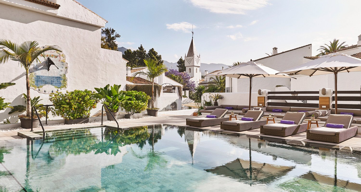 A serene pool area featuring lounge chairs and umbrellas, set against a stylish white building backdrop