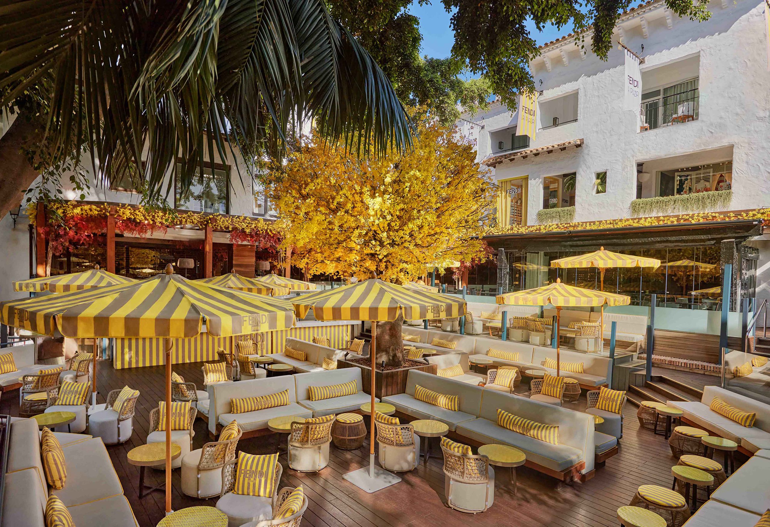 The sunny outdoor patio of Fendi La Plaza is beautifully decorated with yellow umbrellas, perfect for relaxation and enjoyment