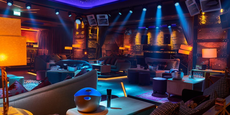 A lively bar featuring a spacious stage and an impressive large light fixture overhead, creating a vibrant atmosphere