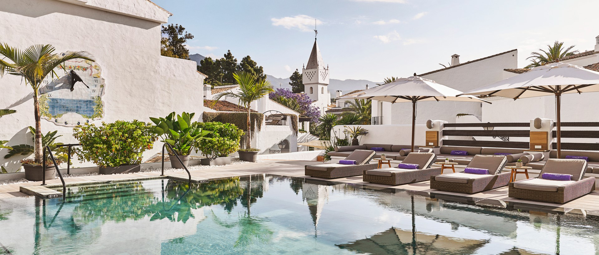 A refreshing pool surrounded by lounge chairs and umbrellas, located in front of a sleek white building, ideal for leisure