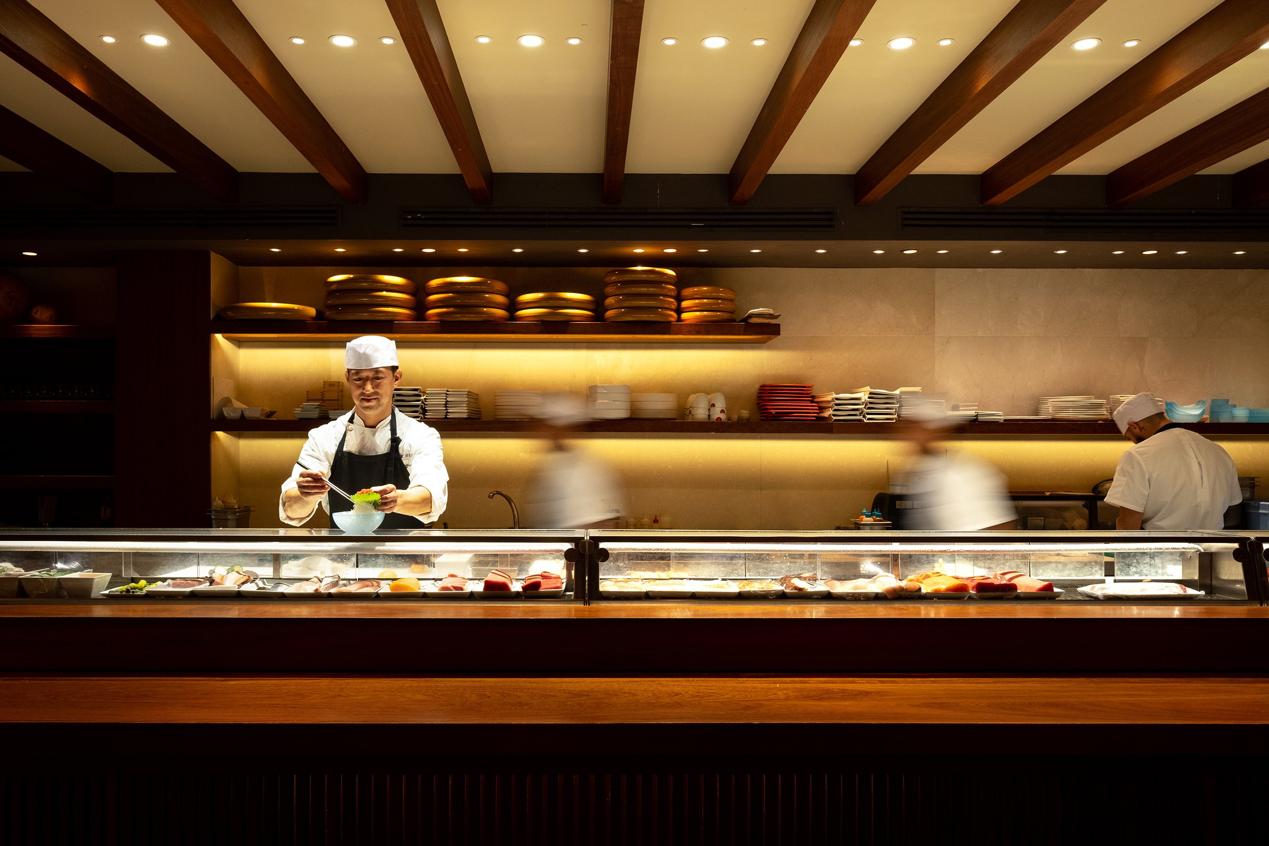 A sushi chef stands proudly at a counter, showcasing beautifully arranged sushi and fresh ingredients ready for preparation