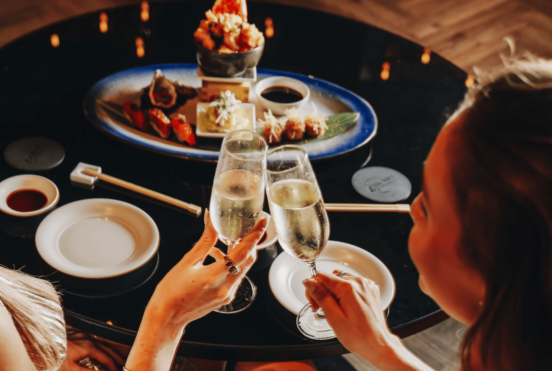 Two women raise their champagne glasses in a toast at a restaurant, enjoying a delightful celebration together.