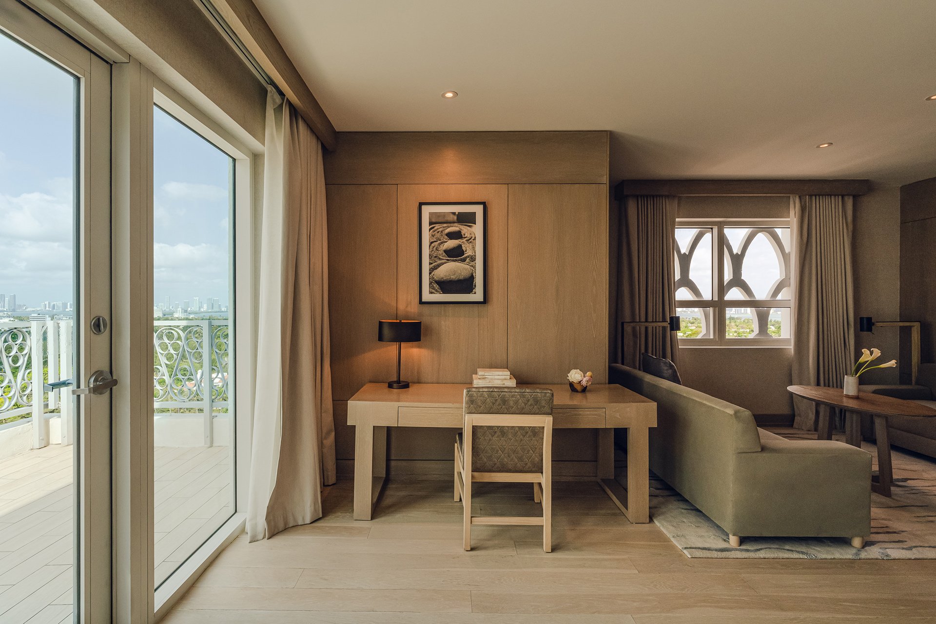 wooden desk, long khaki coloured couch and tea table with balcony