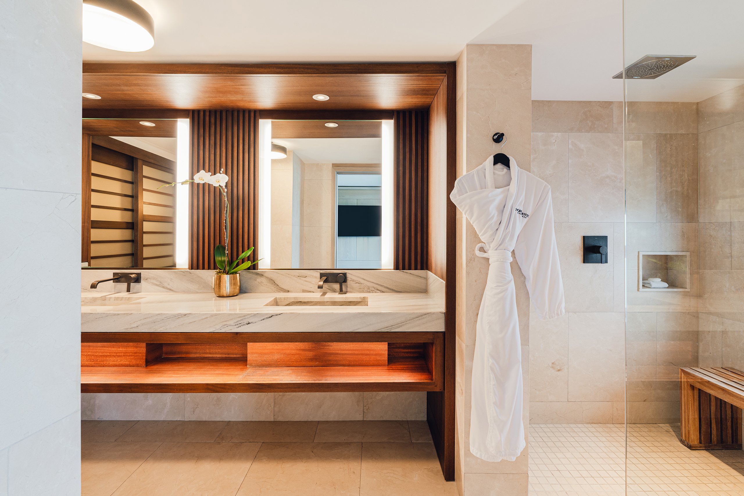 White modern sink, nobu bathrobe, and walk-in shower in white toned bathroom