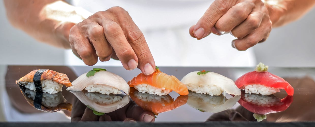 A person placing an array of sushi on a table, featuring fresh rolls and sashimi ready to be enjoyed