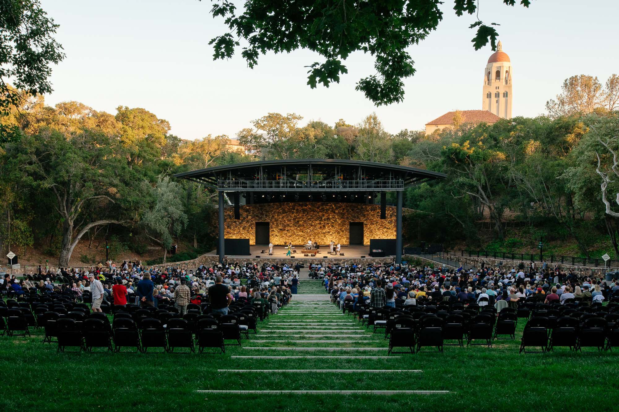 A lively outdoor concert scene with a large crowd in lawn chairs under the open sky