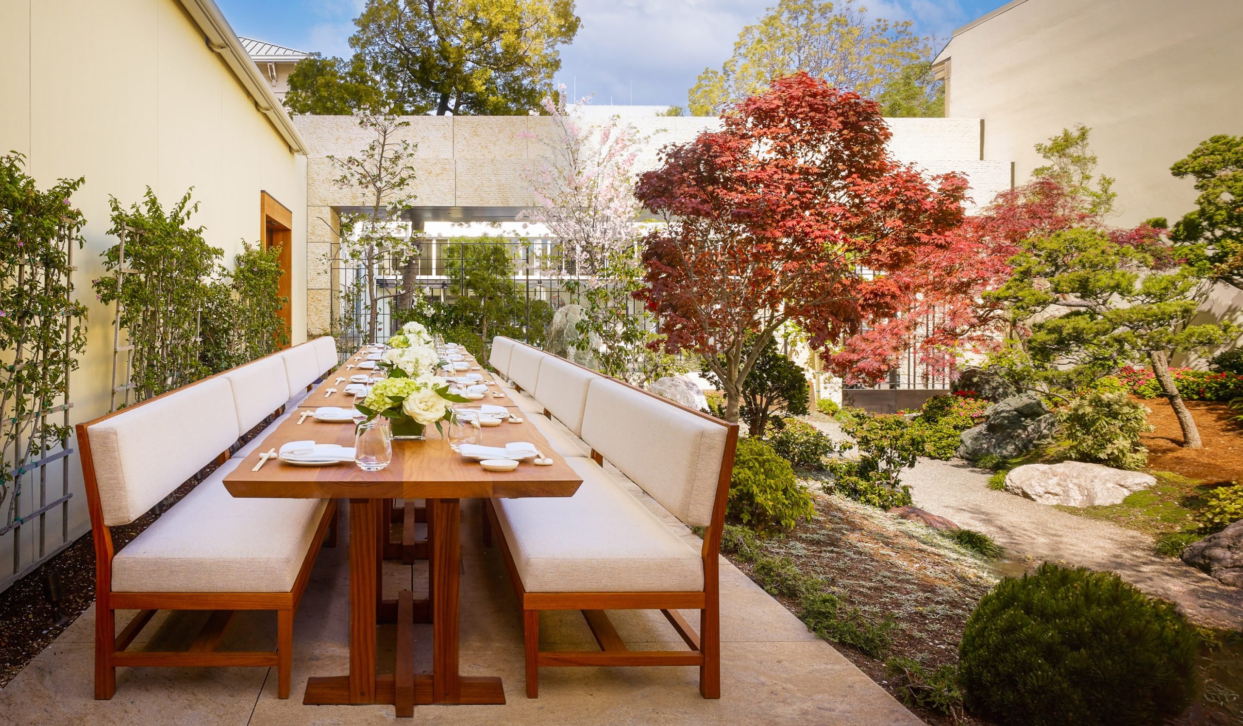 A large wooden table and comfortable ivory coloured chairs in the garden with beautiful trees