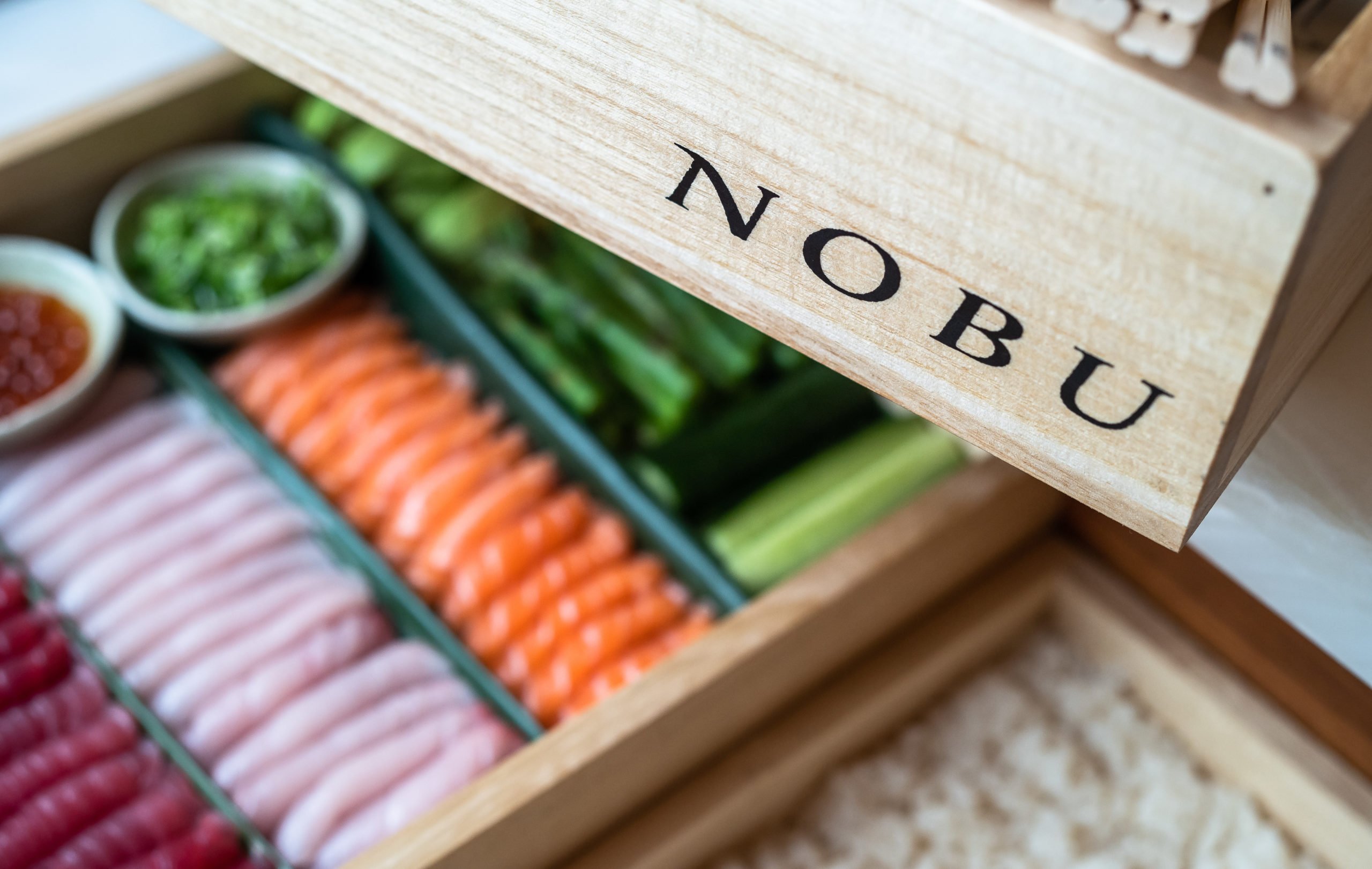 A wooden box filled with colorful sushi rolls and fresh vegetables, ready to be enjoyed