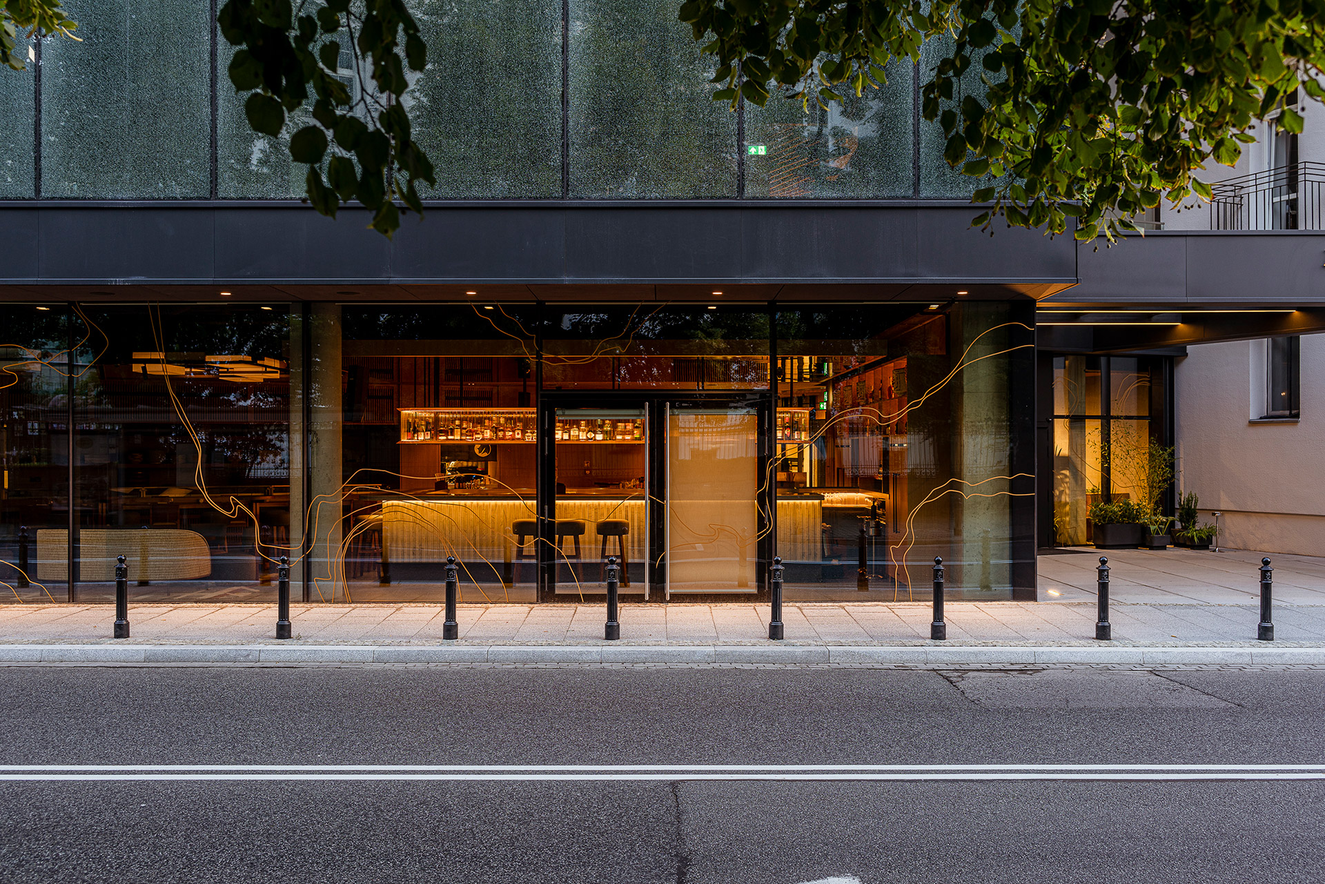 A modern bar restaurant with a glass facade, complemented by a warm street light on the sidewalk.