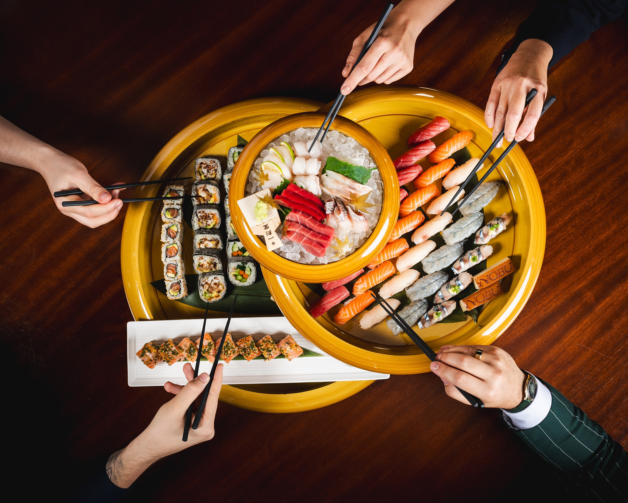 A group of people gathered around a wooden table, using chopsticks to savor delicious sushi plate