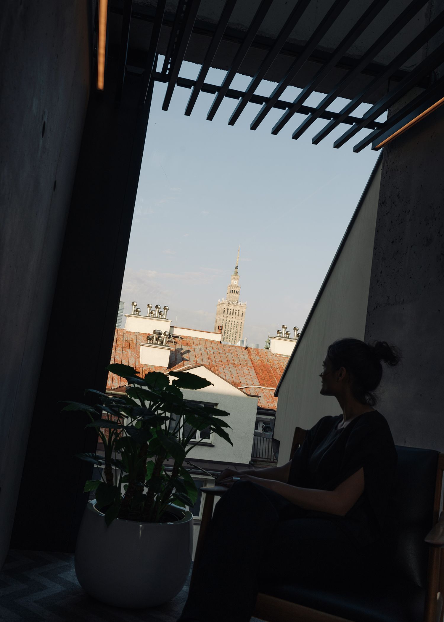 A woman sits in a chair, gazing thoughtfully out the window, lost in her own world.